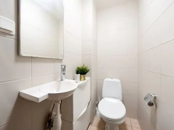 Bright, minimalist bathroom with toilet, small sink, mirror, and modern decor in Tallinn hostel.