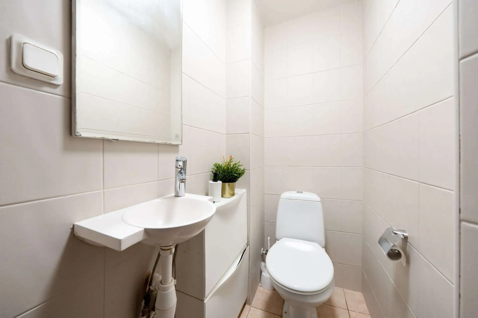 Bright, minimalist bathroom with toilet, small sink, mirror, and modern decor in Tallinn hostel.