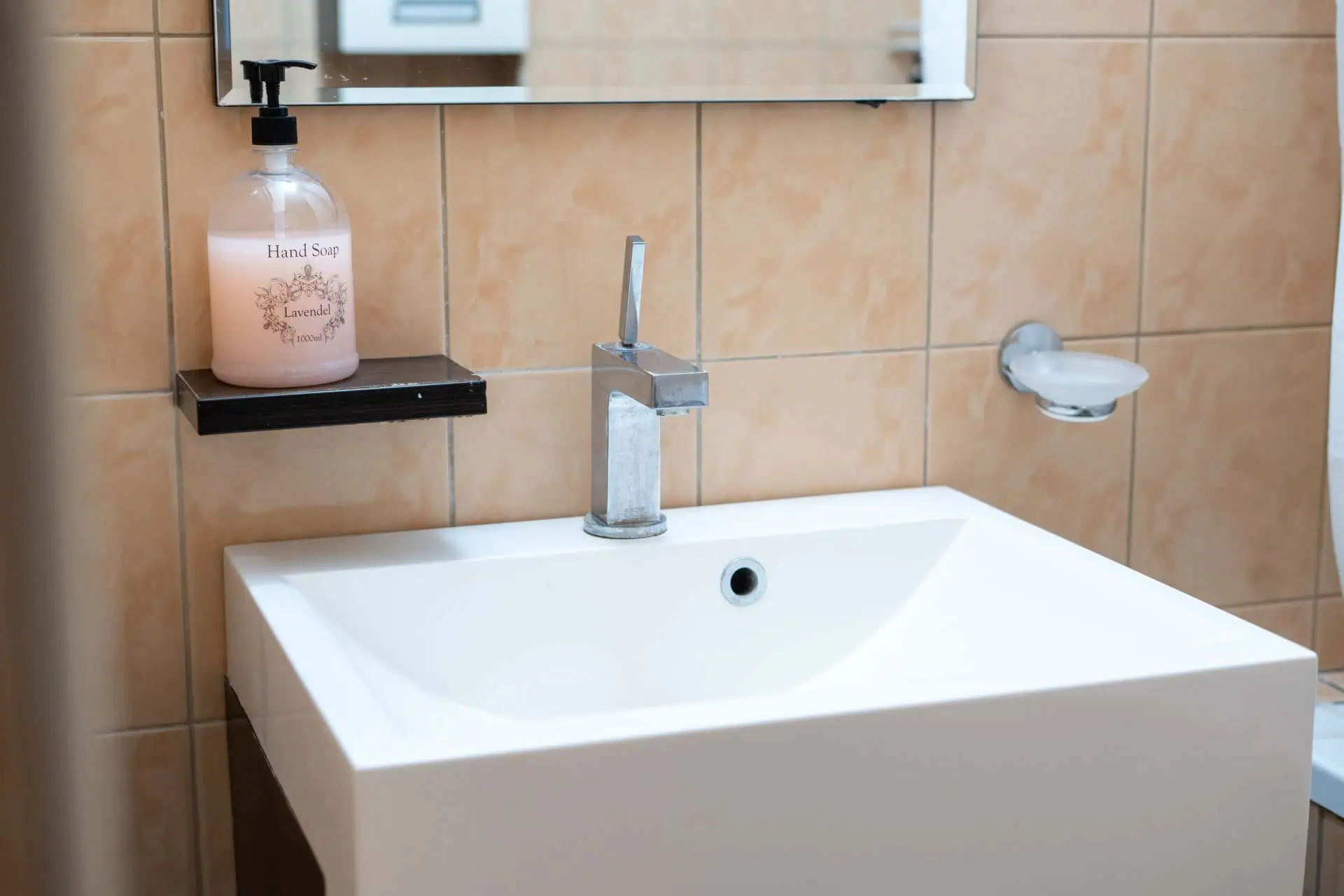 Clean and contemporary hotel bathroom featuring a white sink, modern faucet, and beige wall tiles in Tallinn.