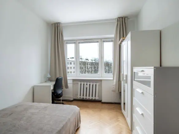 Bright and modern Tallinn apartment featuring a comfortable bed, white furniture, and large windows offering scenic views of the city.