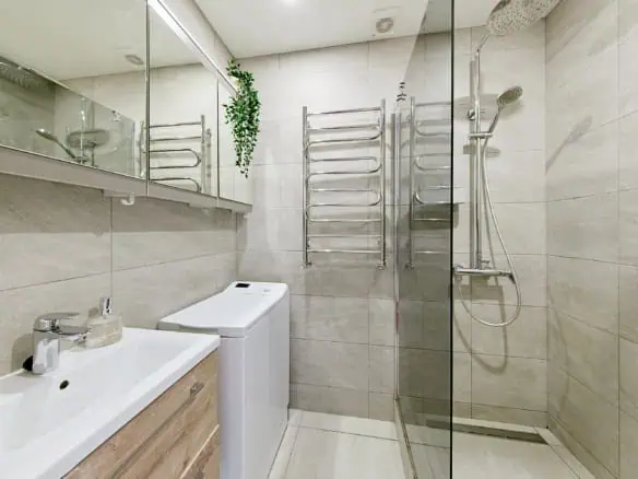 Bright hotel en-suite with walk-in shower, heated towel rack, and compact washing machine in Tallinn.