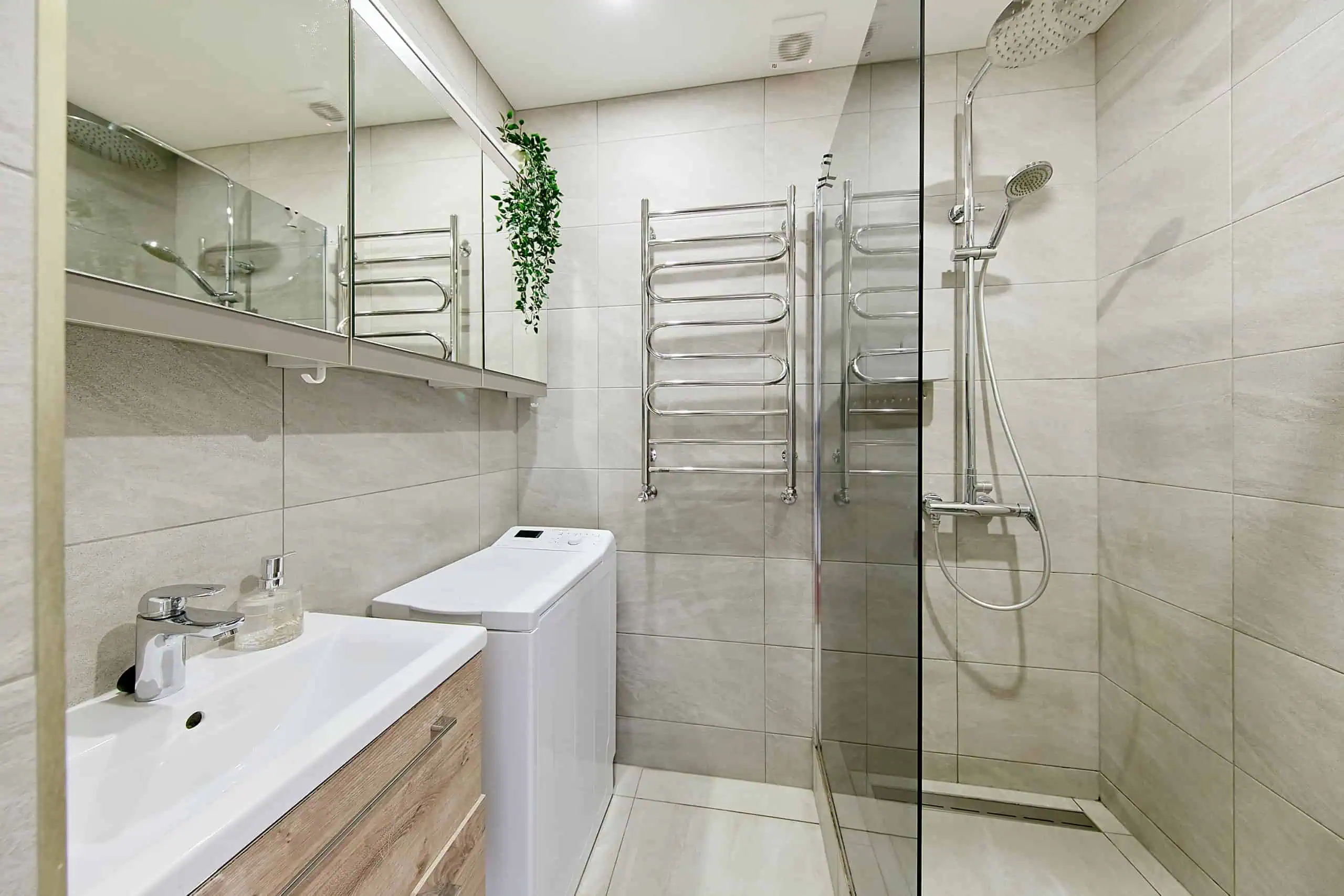 Bright hotel en-suite with walk-in shower, heated towel rack, and compact washing machine in Tallinn.