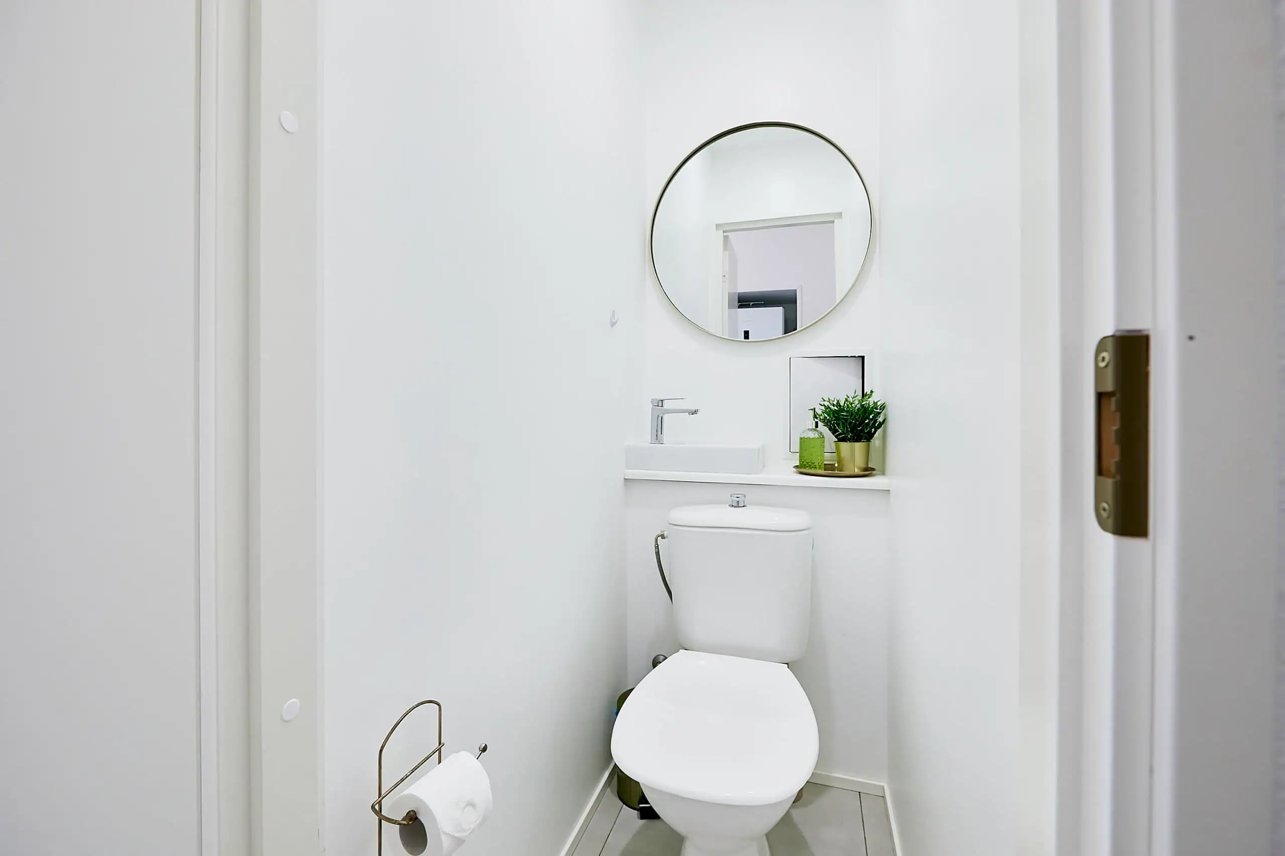 Bright, minimalist bathroom with white walls, round mirror, and small sink in Tallinn hotel.
