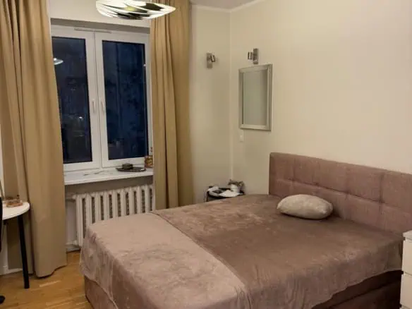 Modern bedroom with beige curtains, soft bedding, and warm lighting in Tallinn's Koolrooms Tallinn.