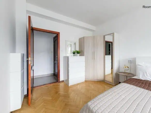 Bright contemporary guest room with white walls, cosy bedding, wardrobe, and bedside lamp.