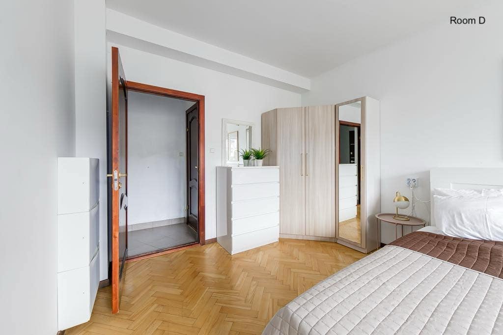 Modern Tallinn studio bedroom with minimal decor and wooden flooring. Bright contemporary guest room with white walls, cosy bedding, wardrobe, and bedside lamp.