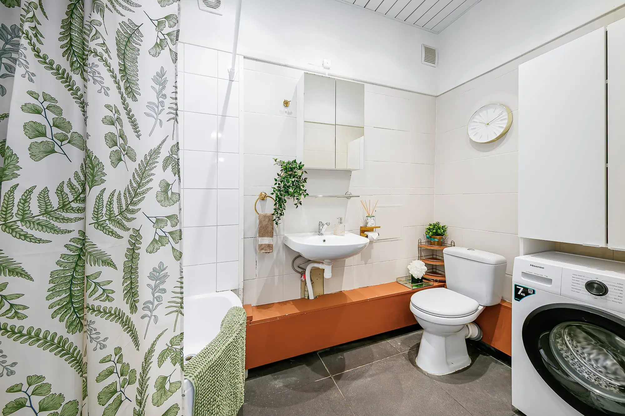Bright, clean guest bathroom with plant accents, white tiles, and practical amenities.