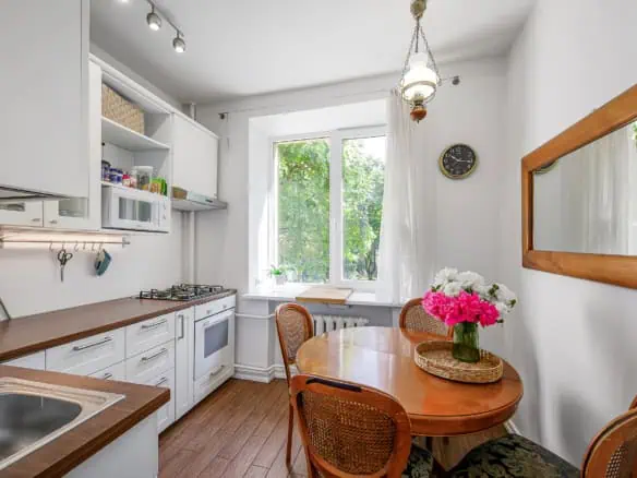 Bright Tallinn apartment kitchen with white cabinets and wooden dining table, perfect for guests at Koolrooms Tallinn.